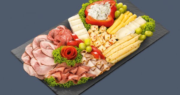 Eine Platte mit verschiedenen Käsesorten und Wurstsorten dekoriert mit Salat, Weintrauben, Tomate und Paprika