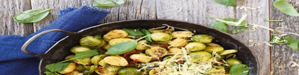 Die Grafik zeigt angebratenes Gnocchi und Rosenkohl in einer Pfanne. Zwischen den beiden Zutaten sind getrocknete Tomaten und Spinat zu sehen. Garniert wurde mit geriebenen Käse.