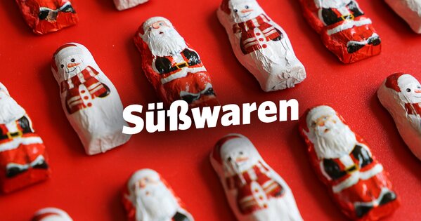 Auf rotem Hintergrund liegen mehrere Schoko-Weihnachtsmänner und Schneemänner ordentlich in Reihen nebeneinander platziert.