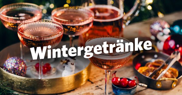 Auf einem Holztisch steht ein gold-weißes Tablett mit pinken Cocktails, umgeben von Weihnachtsdeko und getrockneten Orangenscheiben.