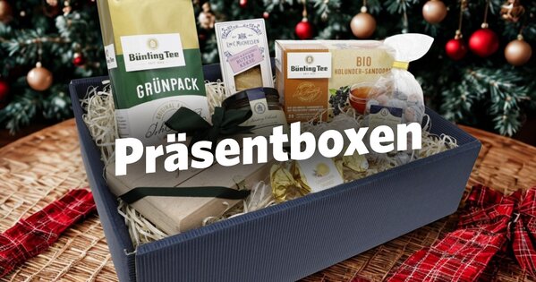 Eine Präsentbox mit Bünting-Tee-Artikeln steht auf einem Korb mit rot-karierten Bändern. Dahinter ein geschmückter Weihnachtsbaum.