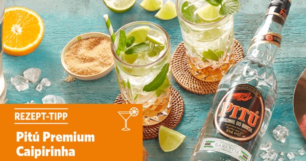 Blauer Tisch mit zwei Cocktail-Gläsern, Rohrzucker, einer halben Orange, Limetten und einer Flasche Pitú