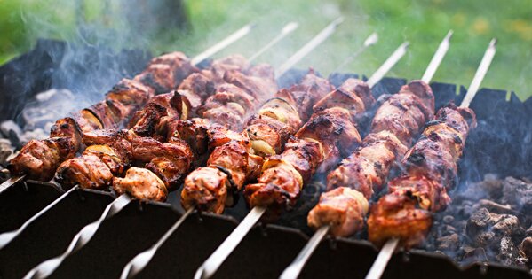 Fleisch und Zwiebeln auf Schaschlik-Spießen über Holzkohle auf einem Grill.