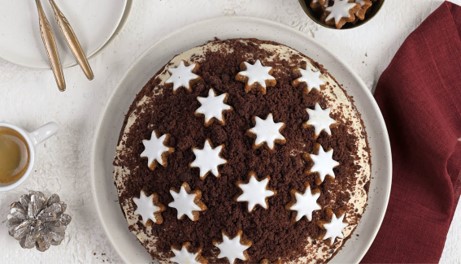 Festliche Adventshügel-Torte mit dunklen Kuchenkrümeln und Zimtsternen auf einer weißen Servierplatte