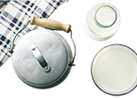 Milchkanne mit einem Handtuch, Milchverpackung und einer Schale Sahne