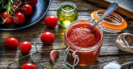 Tisch mit einen Weckglas mit passierten Tomaten, Tomatensträucher, Knoblauchzehe und Oel