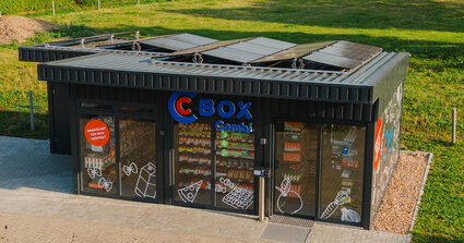 Modernes Containerhäuschen auf Wiese mit Solarpanelen und Illustrationen auf den Scheiben.